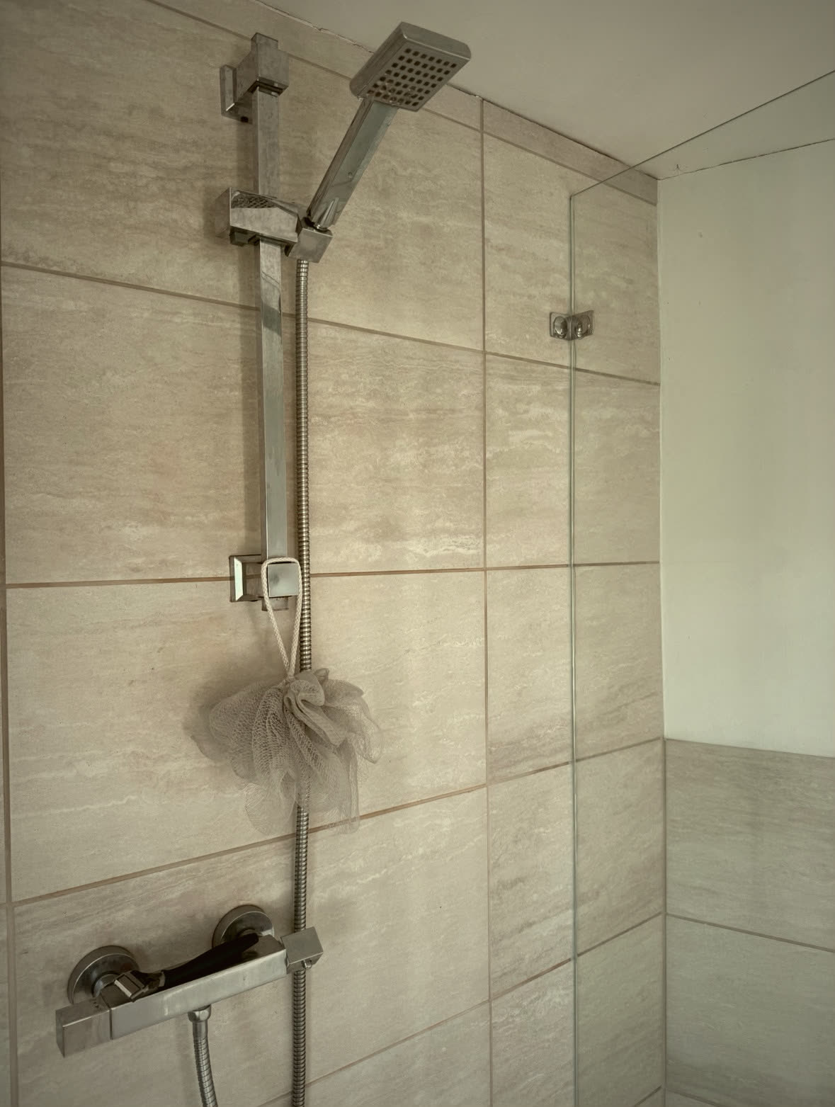 Large-format tiled shower enclosure with glass screen and chrome thermostatic shower