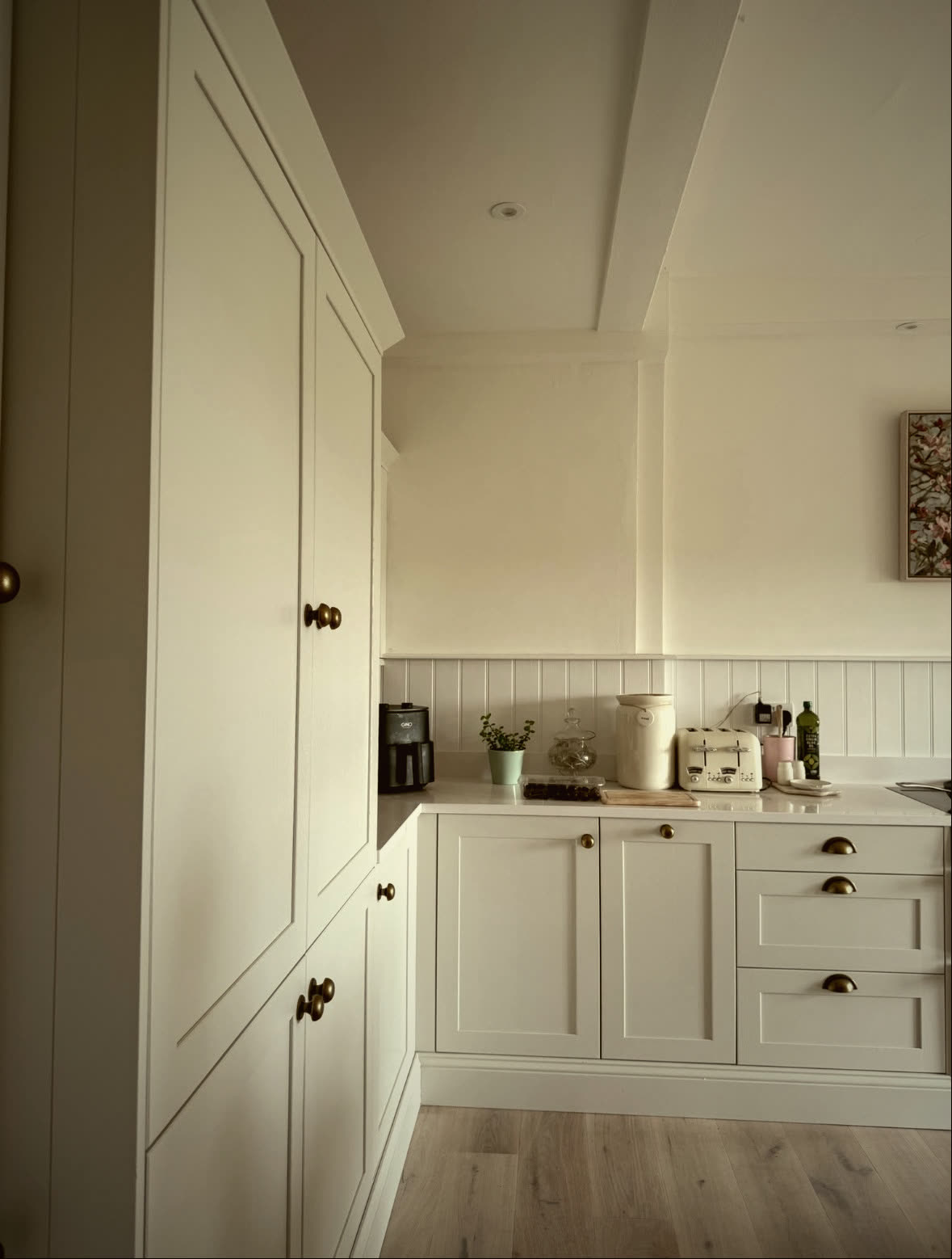 Floor-to-ceiling shaker pantry units with brass knobs in a fitted kitchen