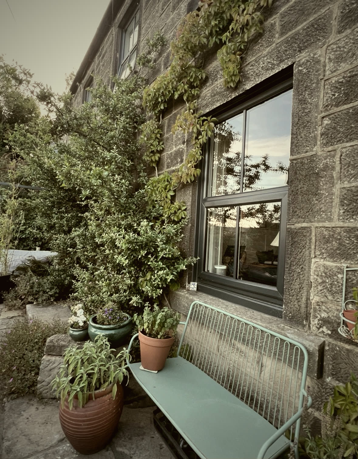 Stone cottage exterior with new slate-grey windows and a planted stone patio