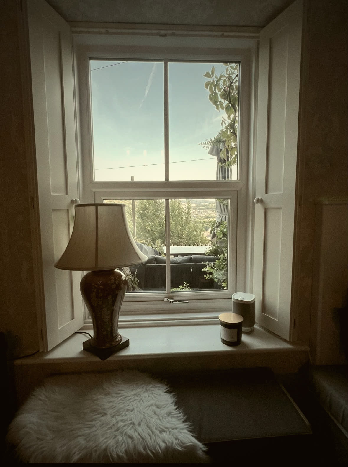 Window seat beneath a restored sash window with panelled shutters and a table lamp